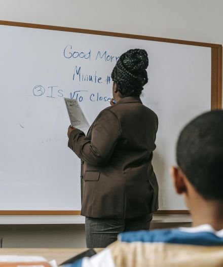 A teacher writes on a whiteboard during a classroom lesson, engaging with students.