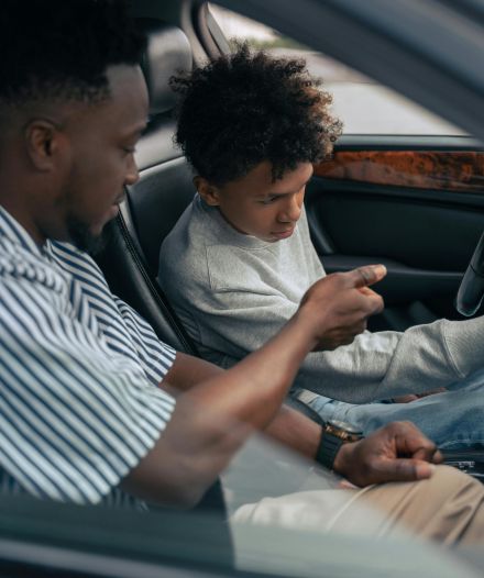 A father and son sit in a car, focusing on driving lessons inside the vehicle.